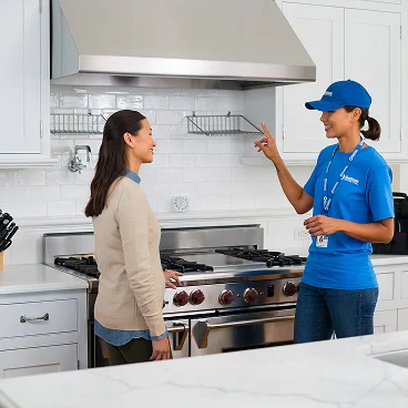 Home service professional consulting with a homeowner about kitchen work near a stove and range hood.