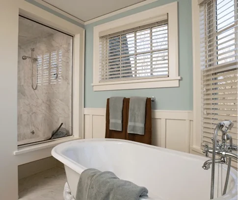 Bright bathroom with a freestanding tub, a glass-enclosed shower, and two towel-covered racks beneath window blinds.